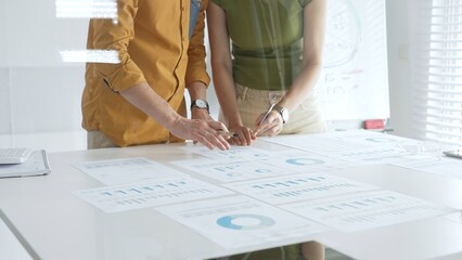Business professionals analyzing financial reports, pointing at charts during collaborative meeting, discussing data with focused professional demeanor