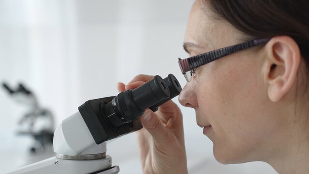Female researcher focusing on a microscope lens, analyzing scientific samples in a sterile lab for medical innovations. Medicine and science concept - Powered by Adobe