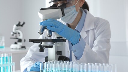A scientist in protective gear adjusts a microscope lens and accurately analyzes medical research...