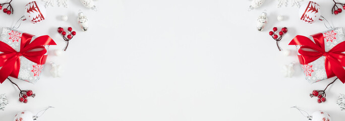 Gift box with red ribbon and winter berries, decorations on white background. Minimalistic festive panoramic composition with copy space. Perfect for Christmas cards, banners, and seasonal advertising