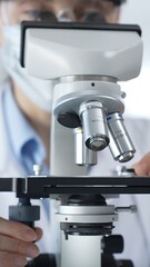 Female scientist wearing lab coat and protective glasses using a modern microscope in a laboratory setting, conducting research and experiments, close up. Health care, medicine and science concept