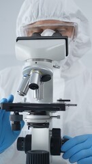 Male scientist virologist wearing hazmat suit, mask, and blue gloves, diligently working at a microscope in a laboratory researching viruses. Medicine and science concept