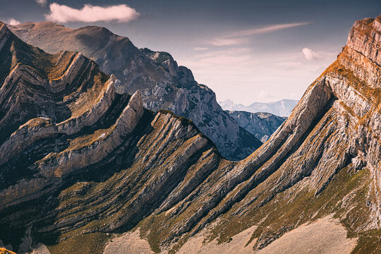 Alpine mountains revealing striking folded rock formations and geological strata. Nature landscape with textured peaks under a clear sky - Powered by Adobe