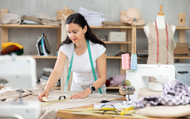 Woman tailor draws dress pattern of product on paper. Craftsman creates paper prototype of parts of future product, drawing paper pattern for dressmaking.