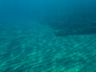 Sunlight shining  the surface and under the blue ocean, sea wave, with clean waters in summer time, Ocean blue underwater with sunrays, underwater blue ocean, sandy sea bottom underwater background.
