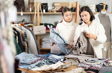Adult female shopper and her daughter buying jeans and trousers in clothing store