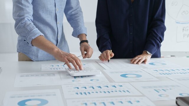 Professional team collaborating, reviewing financial graphs, calculating metrics, discussing performance insights and strategic planning in modern corporate workspace. Business people concept