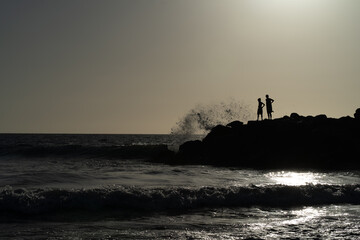 Silhouette of people on the rocks in the sea at sunset