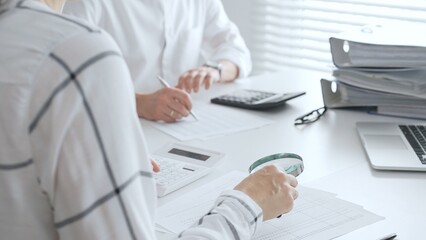 Groupe of accountants collaborating on financial analysis, using a magnifying glass, calculator,...