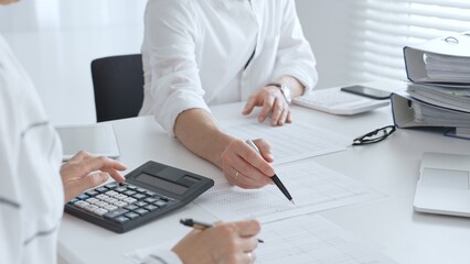 Two accountants collaborating in a well lit office, analyzing financial data and preparing reports...