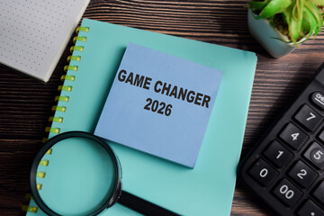 Concept of game changer 2026 write on sticky notes isolated on Wooden Table.