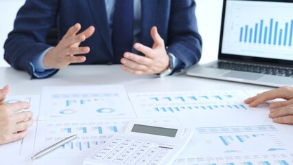 Business professionals collaborating at a conference table, reviewing financial charts and reports, using a laptop and calculator while engaging in discussions about strategy and performance