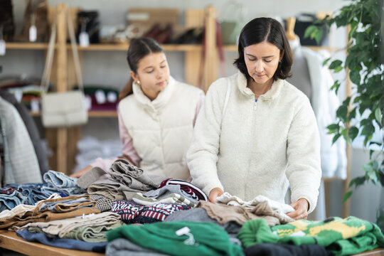 While shopping, mother and teen daughter looks at products in store and selects knitted jumper. Concept of seasonal wardrobe shopping. Client at shopping time leisure activity.