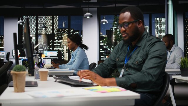 Black coworkers team monitoring forecast data for a new monthly analysis in dark office, utilizing reports and insights to plan reports and statements. Goal setting after hours.