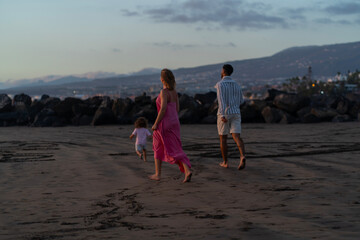 Young family of three having fun on the  on the black sand beach Troya at sunset Tenerife Spain.