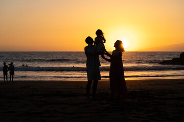 Young family of three having fun on the  on the black sand beach Troya at sunset Tenerife Spain.