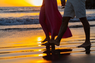 Couple walking on the beach at sunset, holding hands,