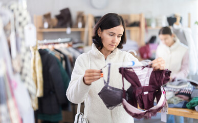 While shopping, woman looks at products in store and selects brassiere. Concept of seasonal wardrobe shopping. Client at shopping time leisure activity.