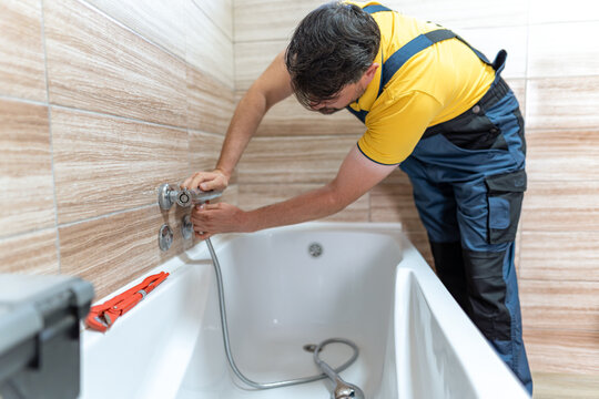 Plumber installing new fixtures in a bathroom tub during daytime work hours