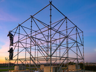 Installation scaffolding and platforms. Erection temporary metal structure outdoors. Construction scaffolding for concerts. Installation of metal scaffolding. Platform under construction at sunset.