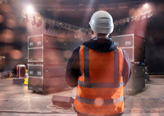 Stage technician in safety vest and helmet supervises equipment setup for concert, managing...
