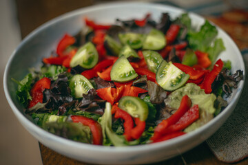A freshly prepared salad featuring sliced green tomatoes and red bell peppers sits in a round ceramic bowl. The colors are vivid against the neutral backdrop.