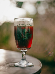 A glass of Irish coffee sits on a table, capturing the sunlight and creating a warm ambiance. The background is softly blurred, enhancing focus on the drink.
