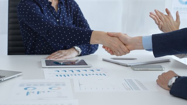 Business people shaking hands at a meeting, celebrating successful negotiations and signing a contract, with documents, digital tablet, and smartphone on the table. Handshake concept - Powered by Adobe