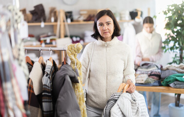Adult woman buyer choosing warm coat or down jacket in clothing store