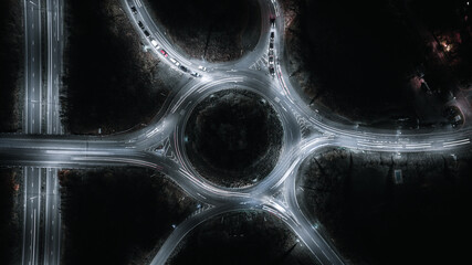 Nighttime aerial view of a roundabout with glowing car light trails creating a dynamic cityscape. © Pavel Babic