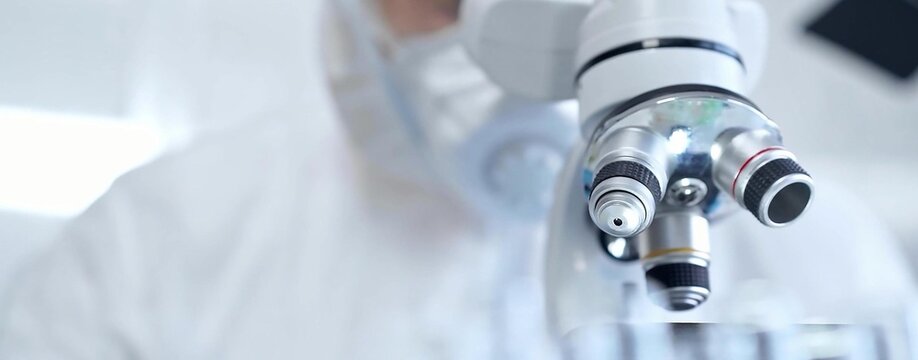 Professional scientist in protective gear is using microscope in a laboratory setting, close-up. Science and medicine concepts - Powered by Adobe