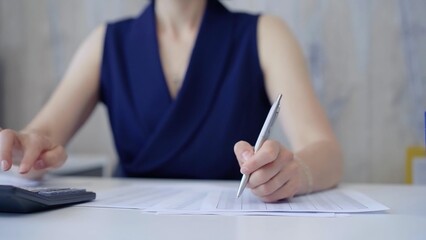 Unknown accountant businesswoman is using calculator and taking notes. Taxes, audit in business