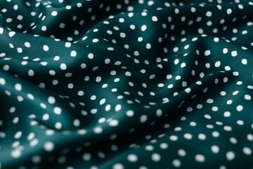 Close-up of dark turquoise colored silk fabric with white polka dots, softly draped to create an abstract background © DariaR