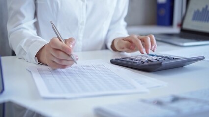 Businesswoman with white blues is using dark calculator and taking notes in her office. Taxes and audit in business