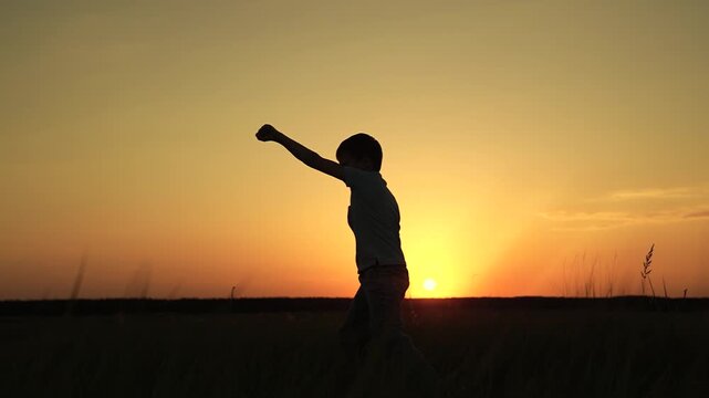 Healthy lifestyle of boy. Boy boxer training punching kicking on meadow. Child kickboxer training outdoor. Child boy karateka training in park, silhouette. Child boxer doing sports in park at sunset.