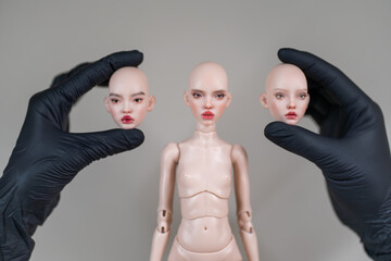 Hands wearing black gloves holding detachable heads amidst doll body. Doll face features unique expressions, highlighting customizable design and craftsmanship of figure