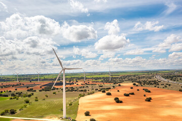 Aerial drone shot of wind turbines spread across vast rural landscape, showcasing renewable energy in harmony with nature under bright cloudy sky emphasizing sustainability and clean power