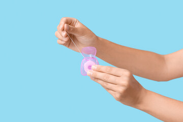 Young woman showing dental floss on blue background