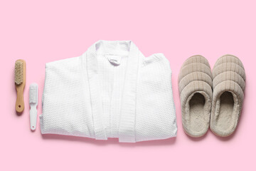 Bathrobe, slippers and brushes foot massage on pink background