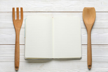 Blank recipe notebook and wooden cutlery on light wooden background