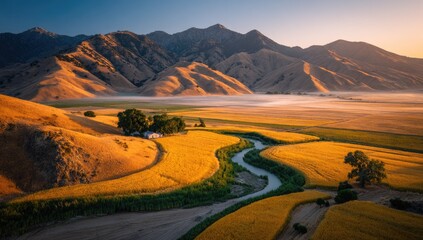 Golden fields and winding river flow through misty valley at dawn.