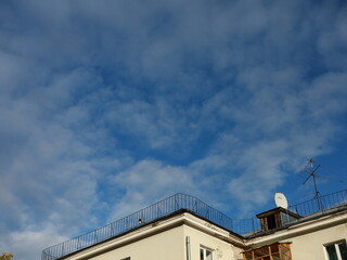 A sky with clouds, some trees, and house rooftops