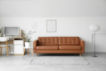 Blurred view of modern office with leather sofa, workplace and floor lamp near white wall