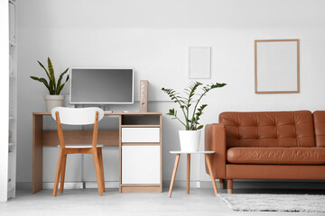 Interior of modern office with leather sofa and workplace near white wall