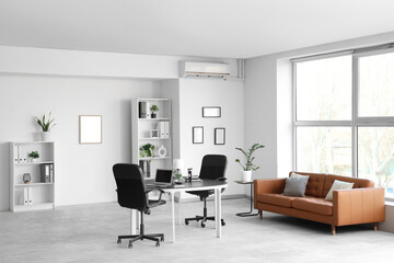 Interior of modern office with leather sofa and workplace near window