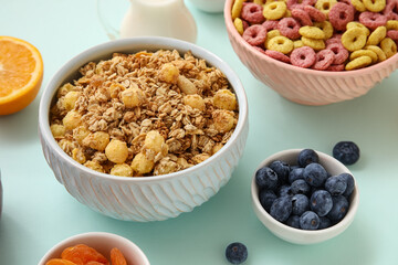 Bowls with cereal rings, granola and ingredients on turquoise background, closeup