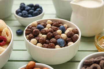 Bowl with chocolate corn balls on green wooden background, closeup