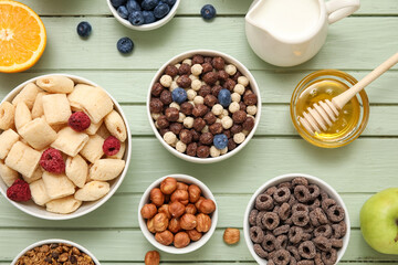 Bowls with different cereals and ingredients on green wooden background