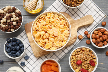Bowls with cornflakes and ingredients on grey wooden background, closeup