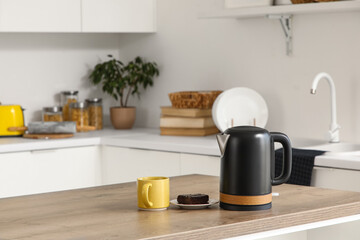 Black electric kettle and cup on table in kitchen, closeup